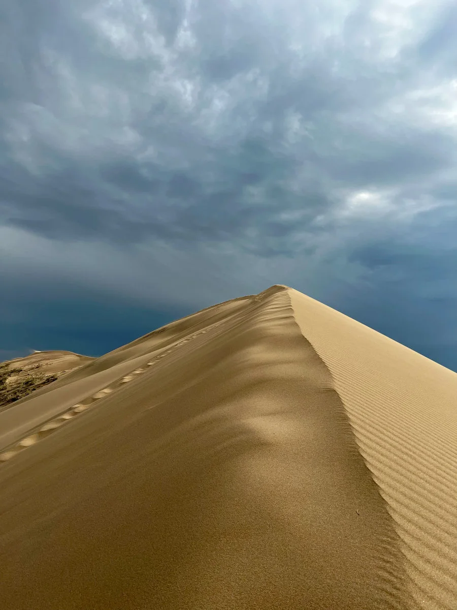 Footprints leading along the ridge of the Singing Dune under a stormy sky